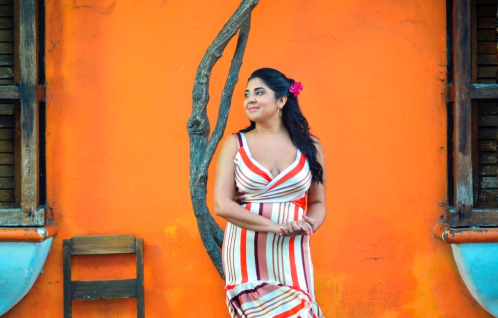 woman w a colorful dree in front of an orange wall