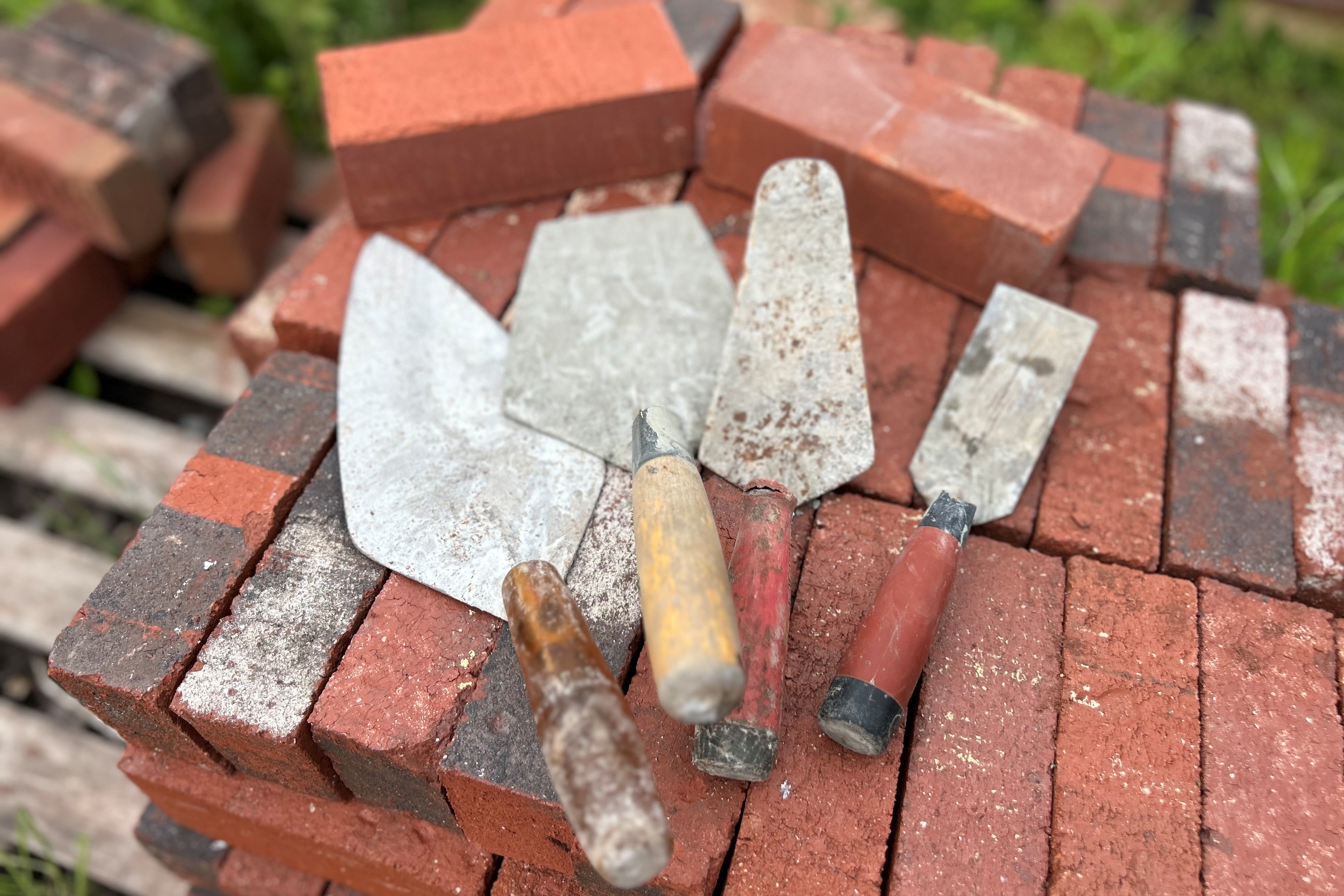 large pile of red bricks w four trowels of different shapes sitting on top of pile