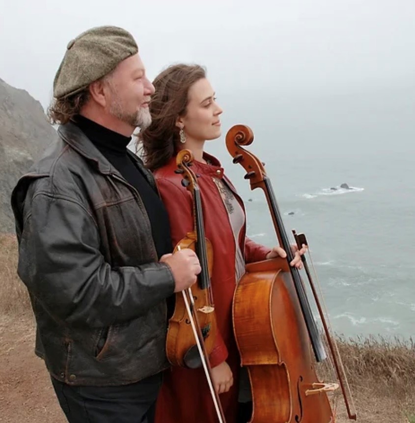 Man and woman holding their string instruments overlooking the ocean 