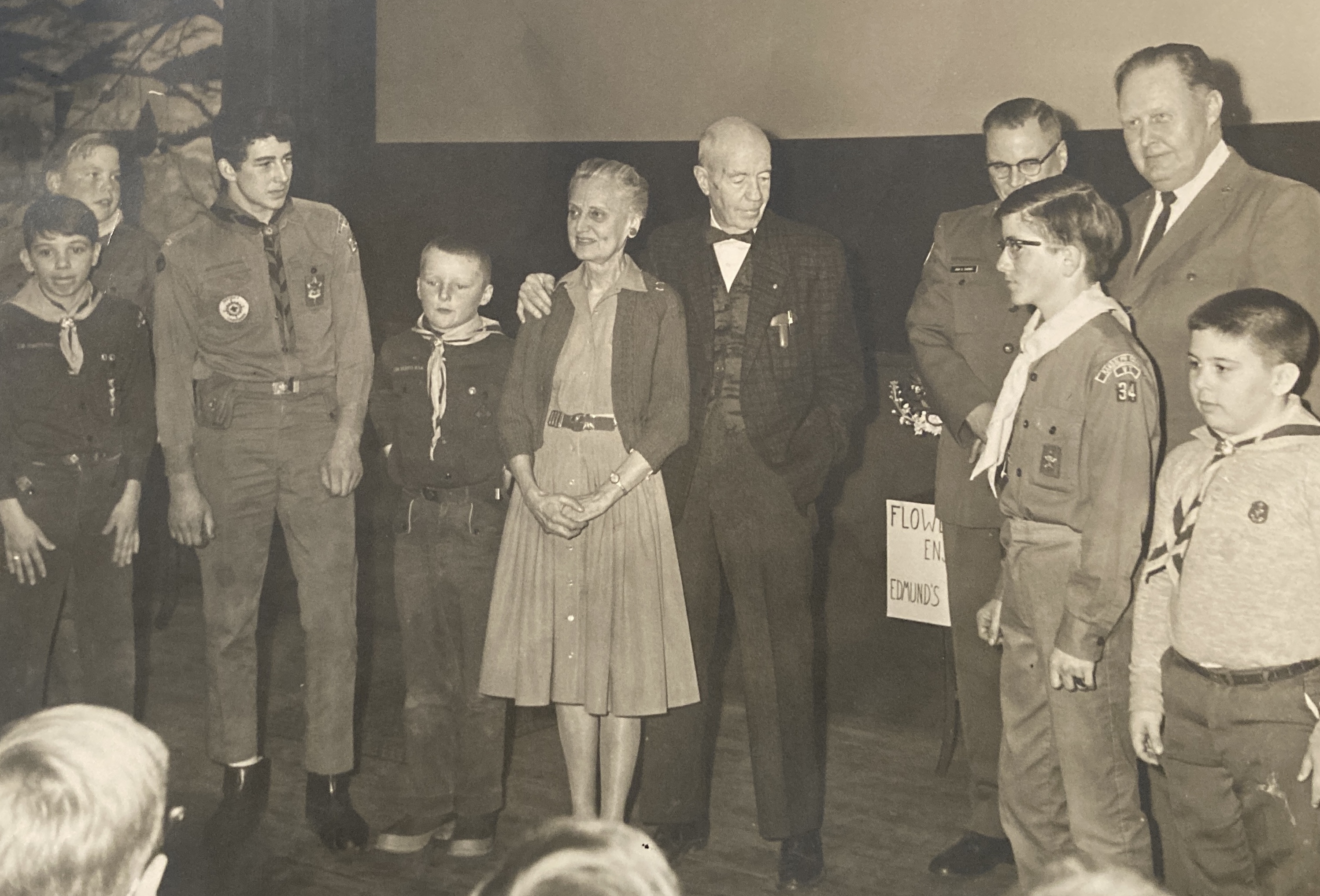 two older people stand in front of hte play house stage surrounded by Boy Scouts.