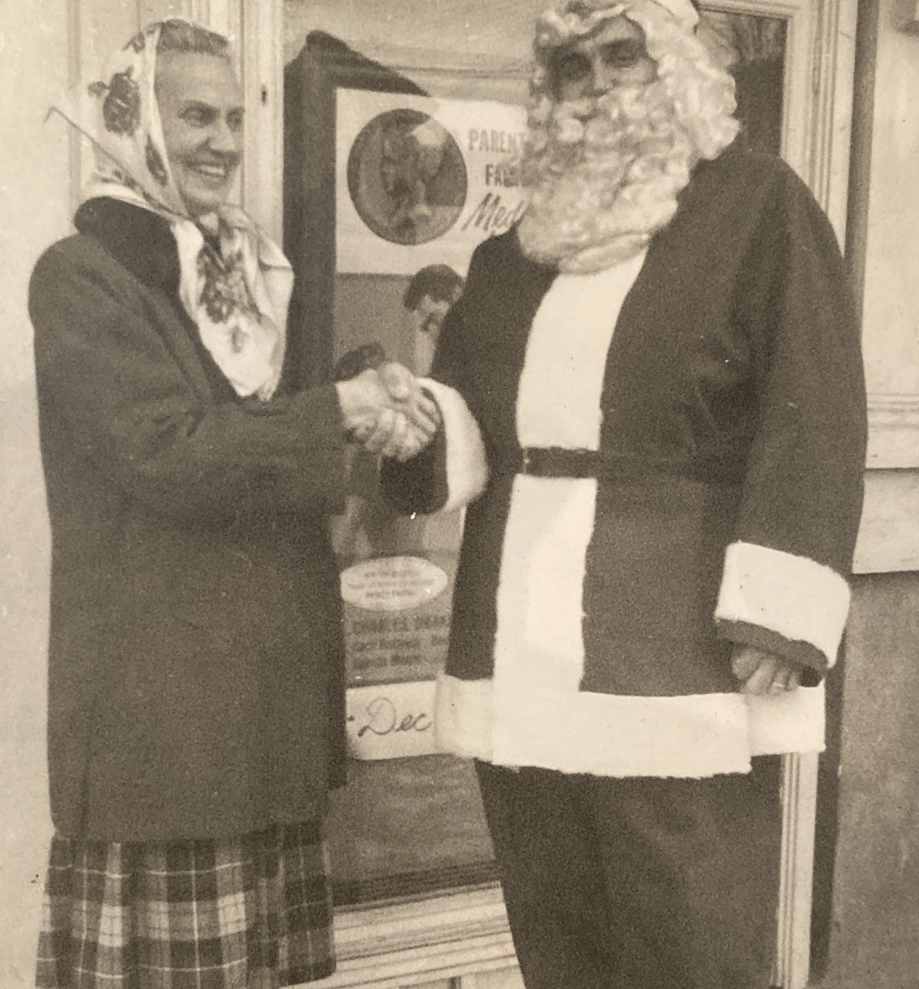 a smiling older woman wearing a scarf shakes hands with Santa outside the movie theater