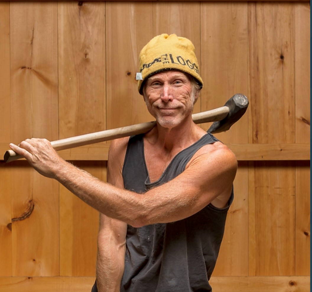 man w tank-top shirt holding an ax over his shoulder w a hat on