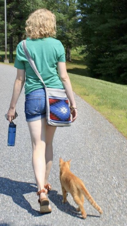 woman walking on a sunny day w a cat beside, following her