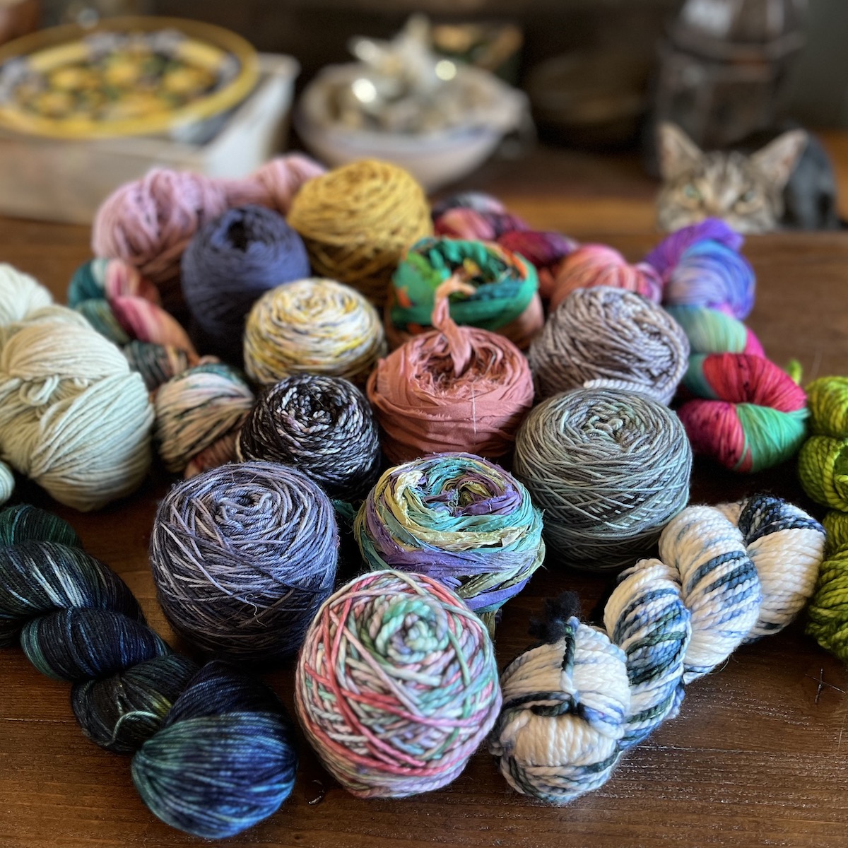 An image of yarn spools on a table. A cat hides in the background.